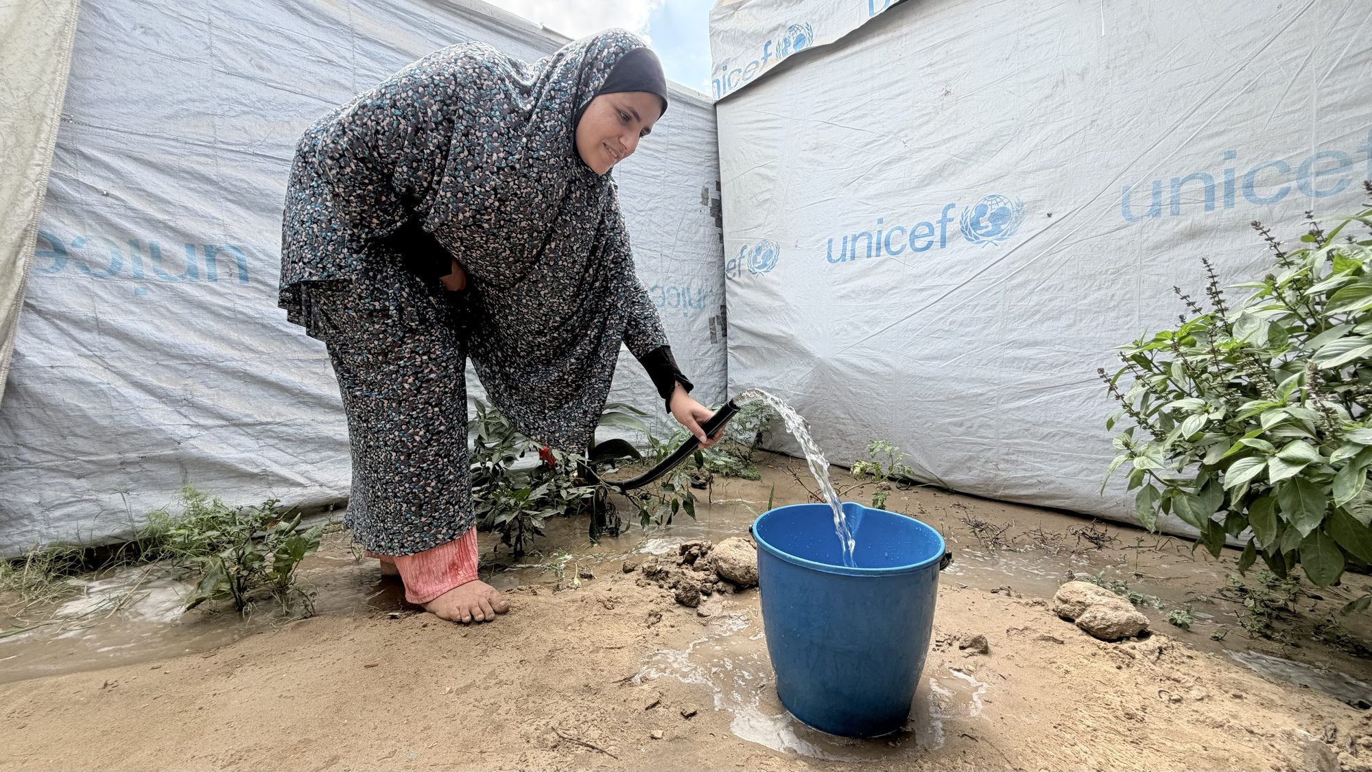 Malak al-Jazzar fills a bucket with water outside the tent