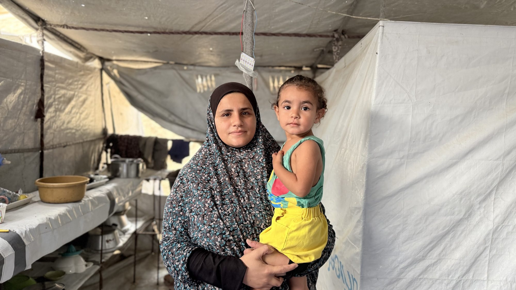 Malak al-Jazzar holds her young daughter inside the family tent