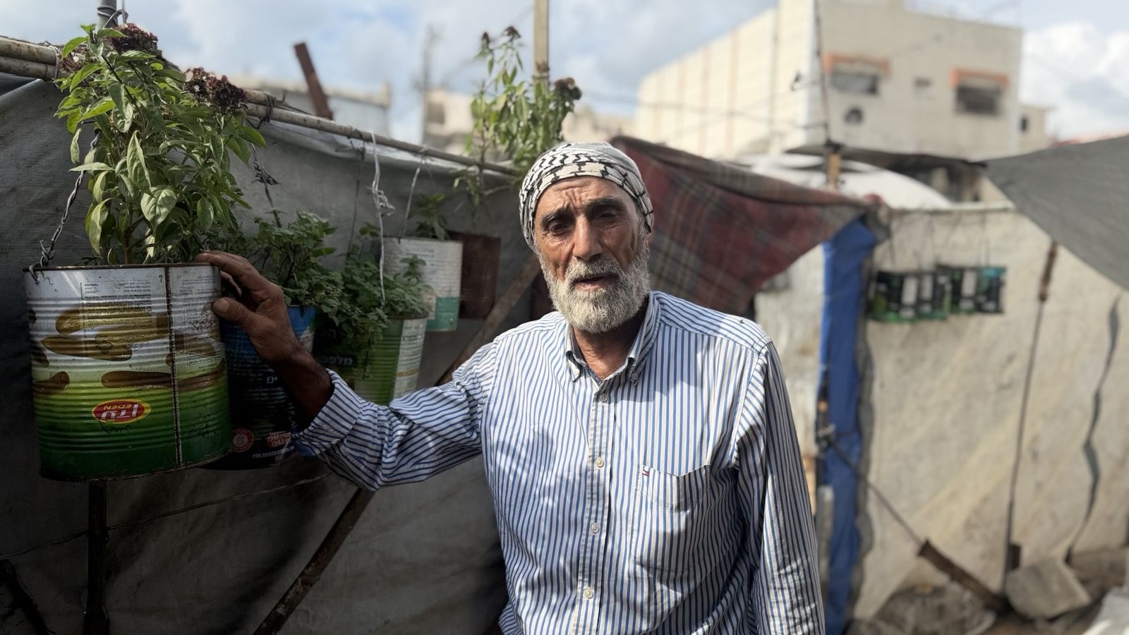Muhammad Sa’dat holds up a plant growing in a tin outside his tent