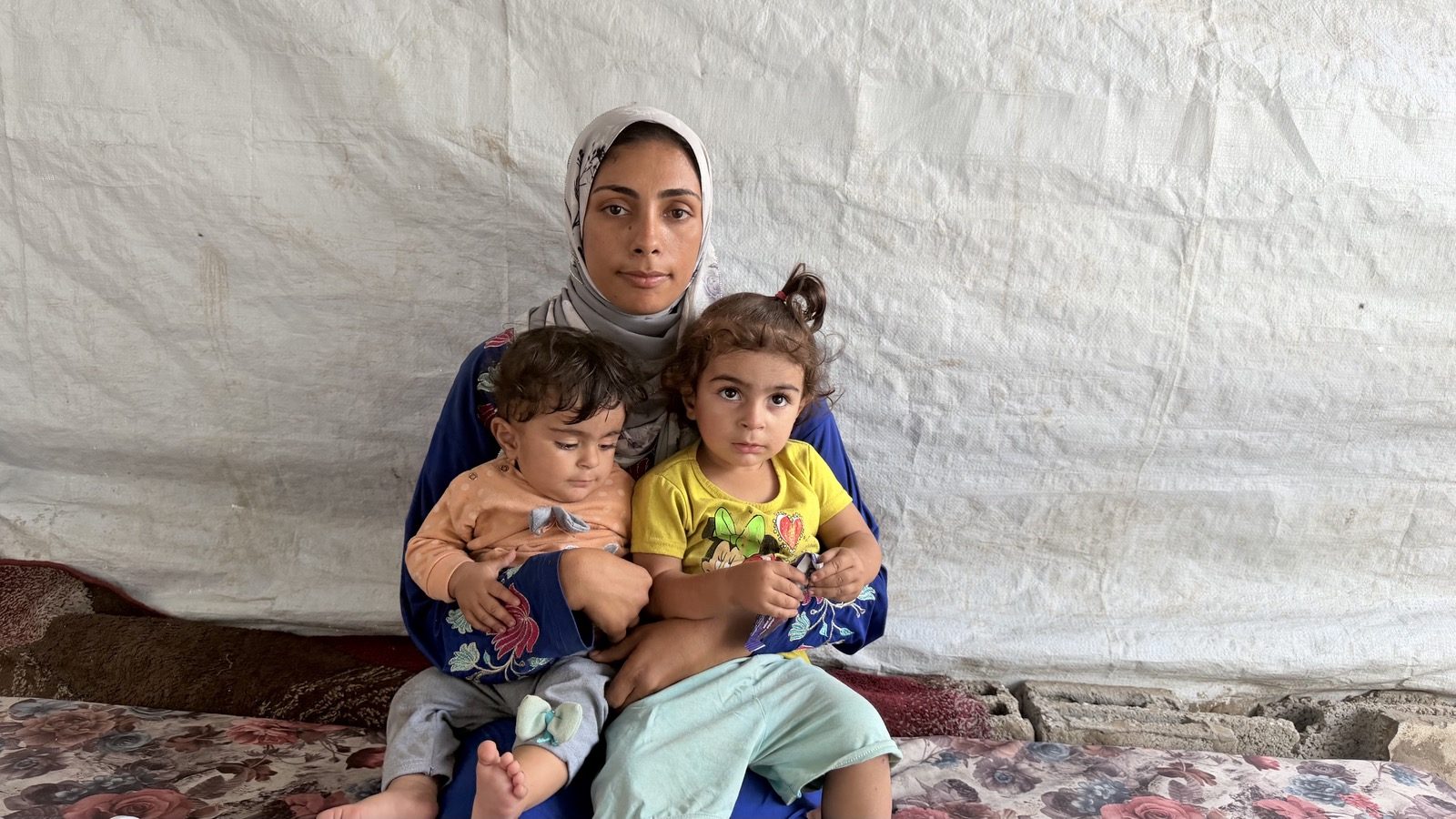 Raneem al-Jadba sits in a tent holding her two young daughters