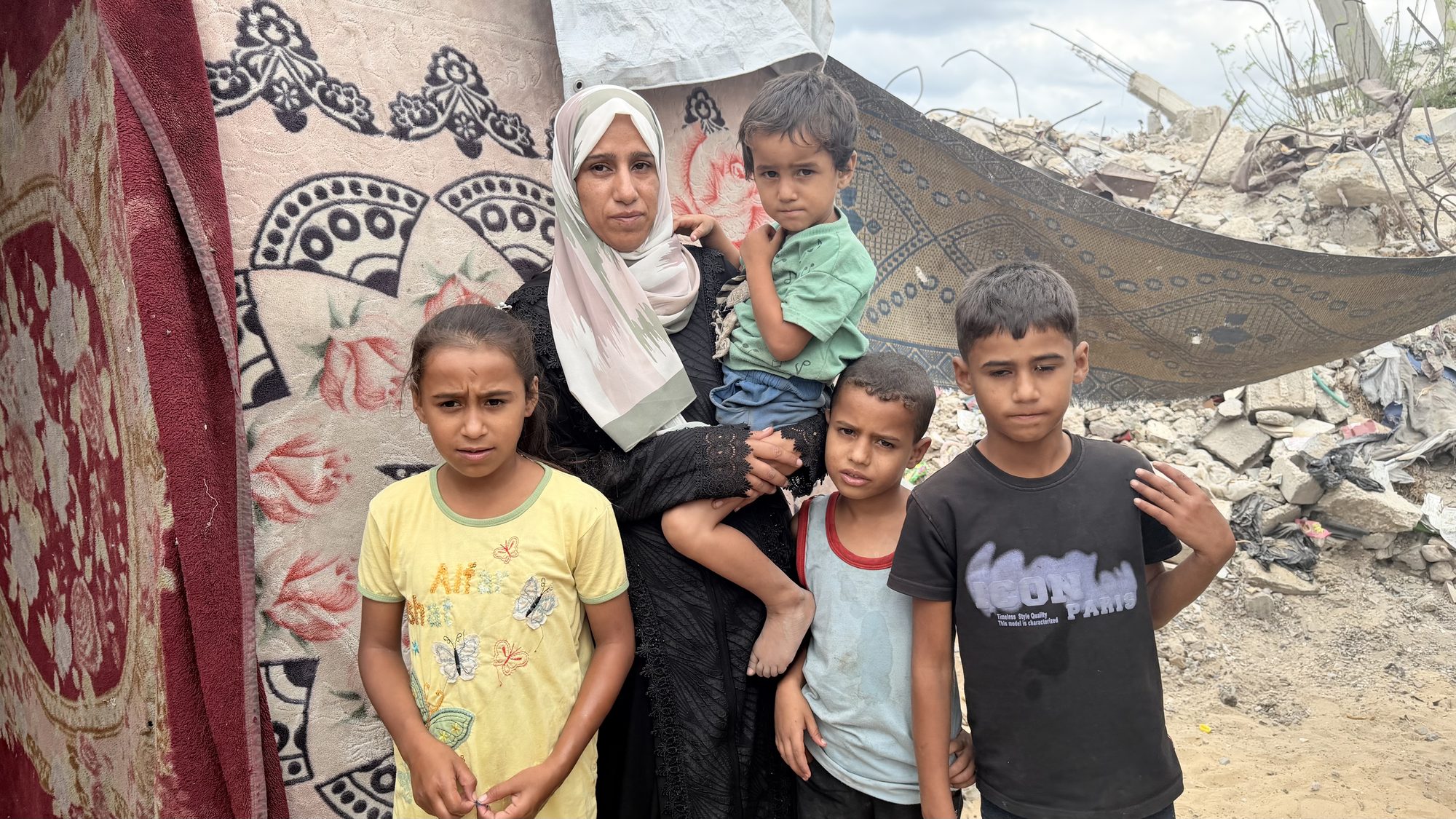 Suhair Abu Nimr with her children in front of a wall next to rubble