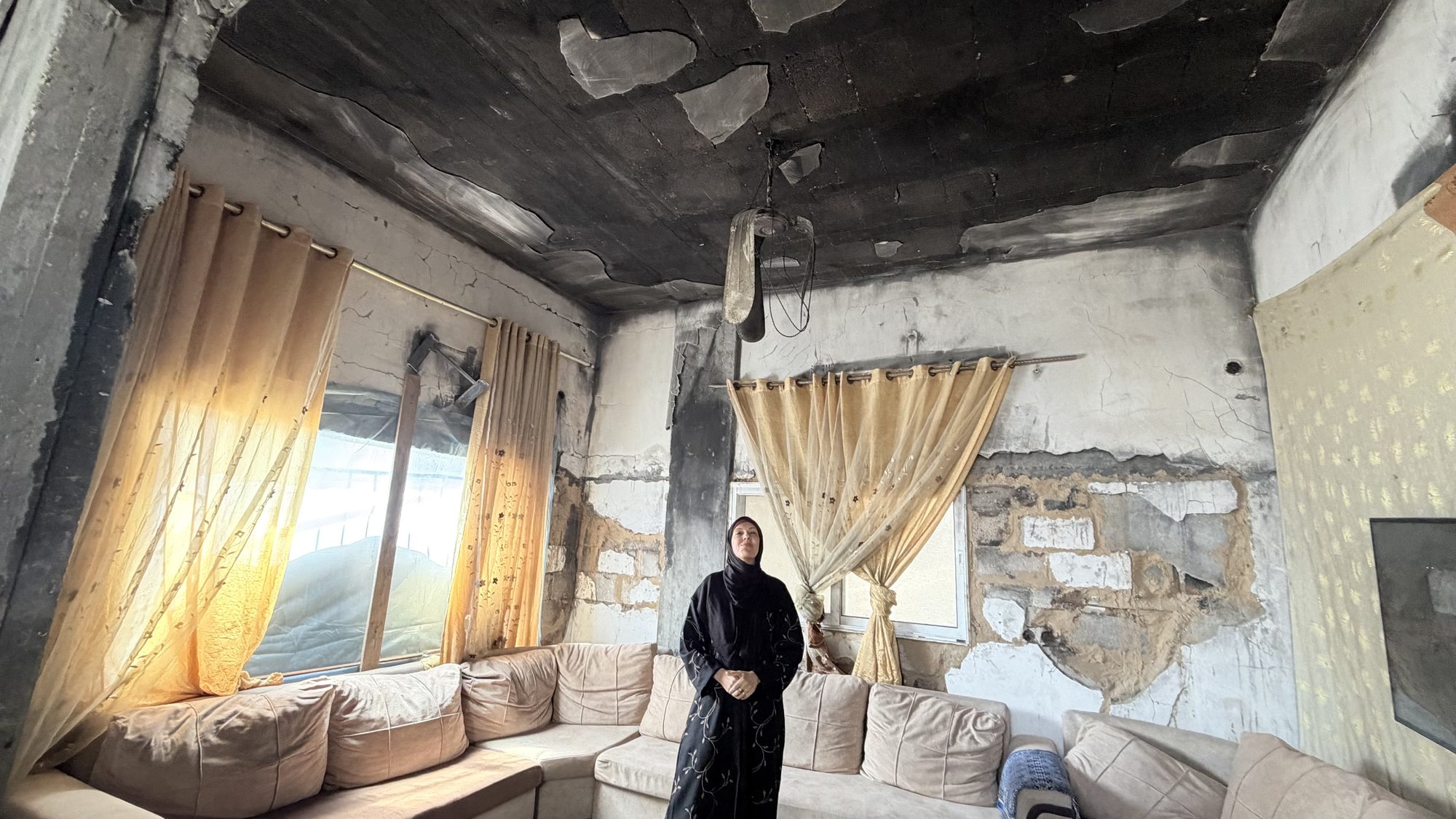 Mai al-Ghalban standing in a burned-out living room