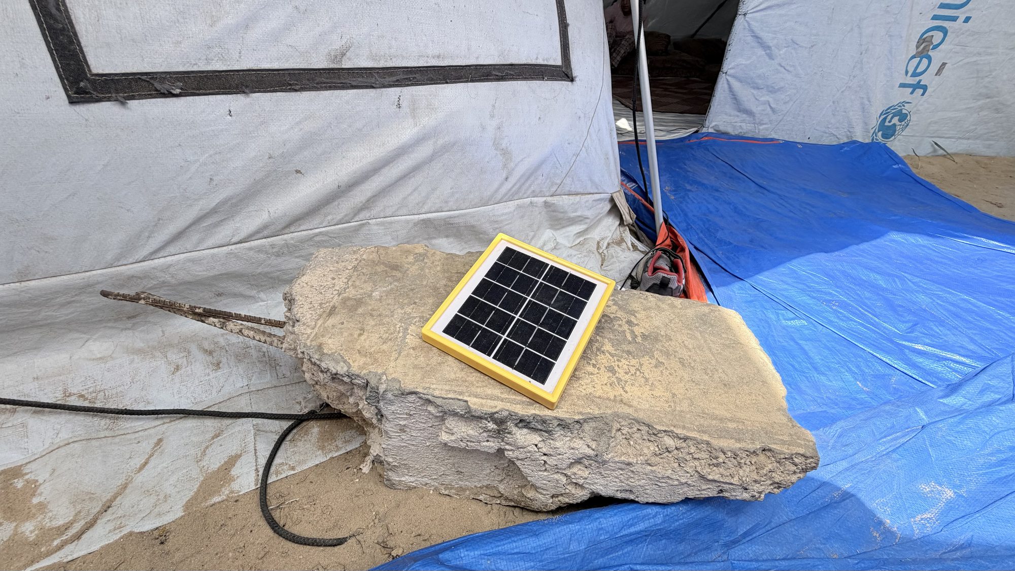 A small solar panel propped on a rock outside the tent